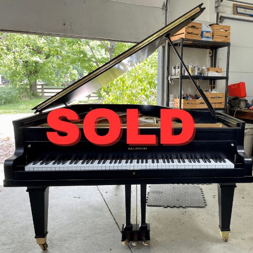 Grand piano with "SOLD" overlay in garage.
